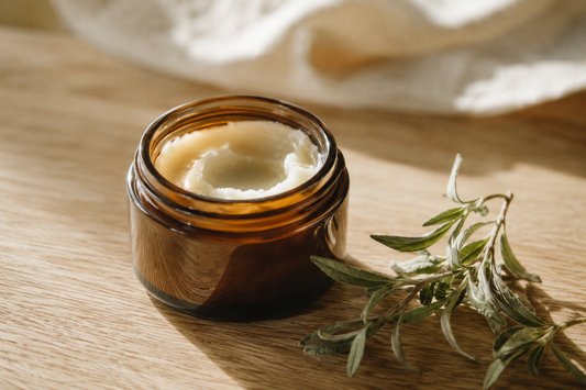 An open amber jar of ivory beef tallow balm on pale oak with soft greenery, an honest look at whether beef tallow causes acne.