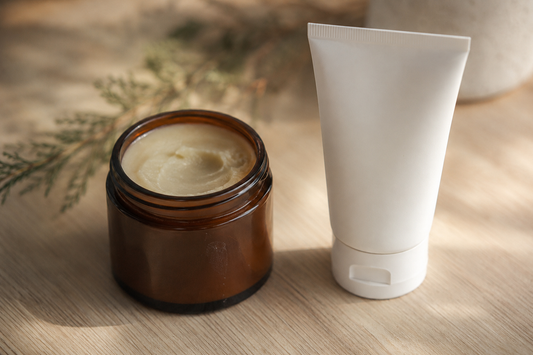 An amber jar of ivory beef tallow balm beside a plain white unbranded cream tube on pale oak, an honest comparison of beef tallow and a conventional moisturizer.